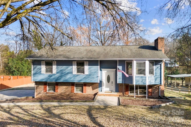 bi-level home with a chimney, fence, and brick siding