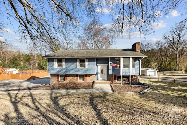 bi-level home featuring brick siding, fence, driveway, a chimney, and a front yard