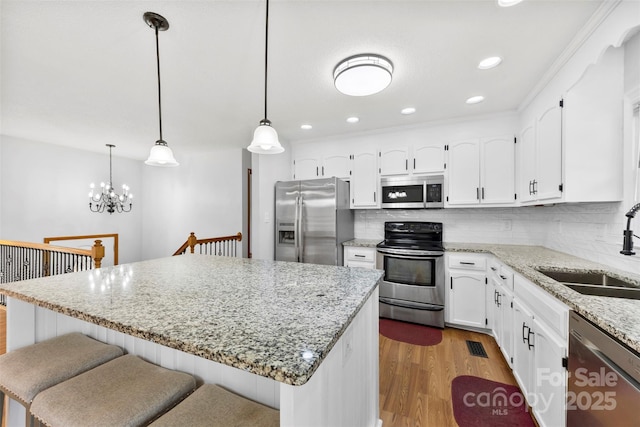 kitchen with hanging light fixtures, a kitchen island, appliances with stainless steel finishes, and a sink