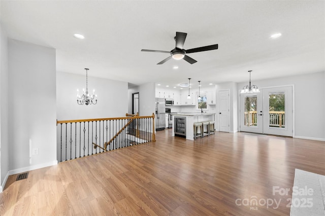 unfurnished living room with recessed lighting, ceiling fan with notable chandelier, wood finished floors, visible vents, and baseboards