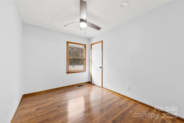 empty room with a textured ceiling, wood finished floors, visible vents, and baseboards