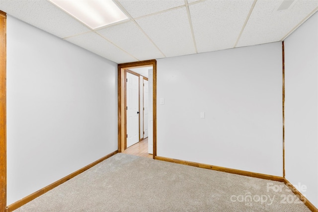 spare room with baseboards, a drop ceiling, and light colored carpet