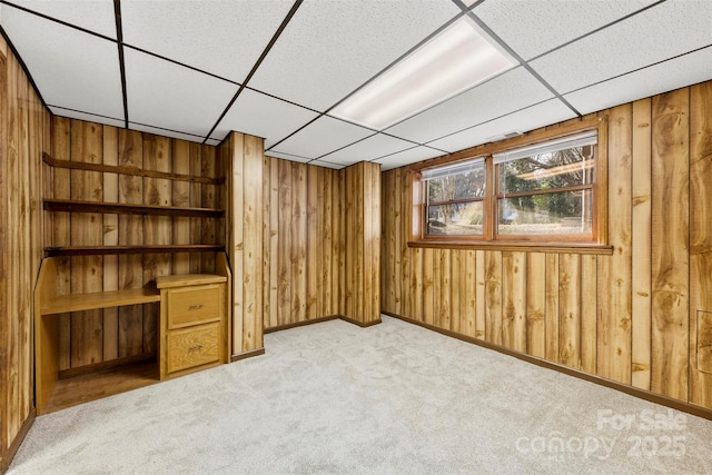 interior space featuring light carpet, wooden walls, and a drop ceiling