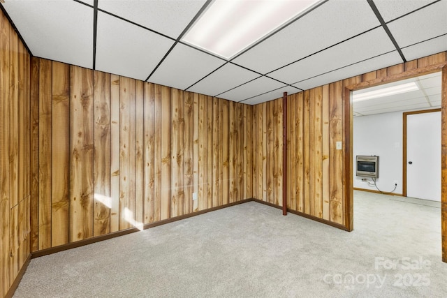 spare room featuring heating unit, wooden walls, a drop ceiling, and light colored carpet