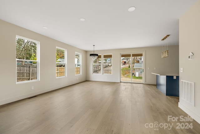 unfurnished living room featuring light wood-type flooring, an inviting chandelier, and plenty of natural light