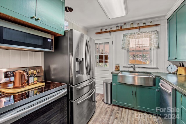 kitchen featuring light wood-type flooring, stainless steel appliances, crown molding, sink, and green cabinetry