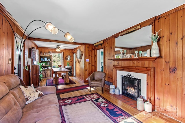 living room featuring ceiling fan, wood-type flooring, wooden walls, a fireplace, and ornamental molding