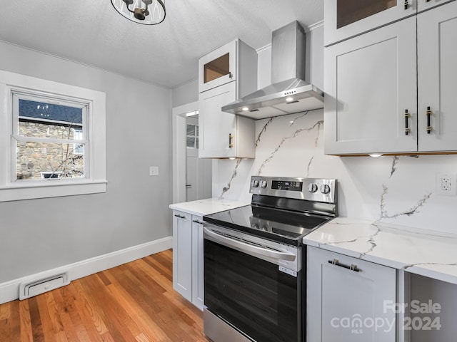 kitchen featuring electric stove, light hardwood / wood-style flooring, wall chimney exhaust hood, decorative backsplash, and light stone counters