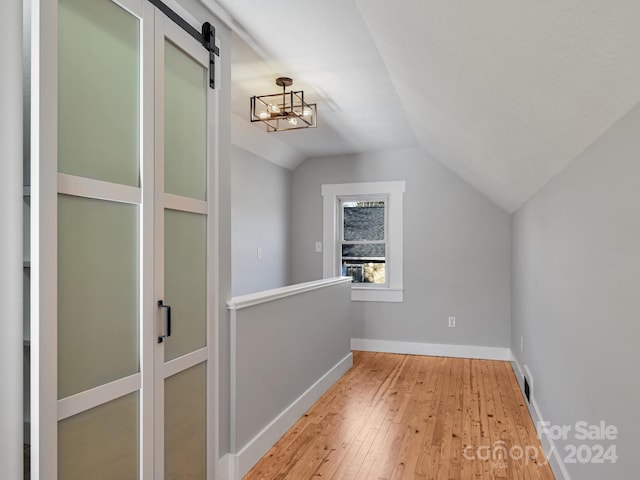 bonus room with light wood-type flooring, a barn door, lofted ceiling, and a notable chandelier