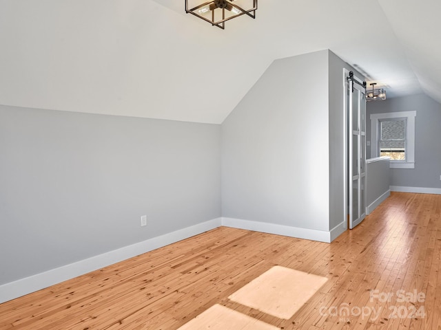 additional living space featuring a chandelier, wood-type flooring, a barn door, and lofted ceiling