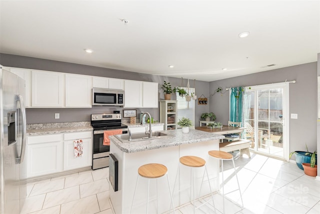 kitchen with a breakfast bar, white cabinetry, sink, stainless steel appliances, and a center island with sink