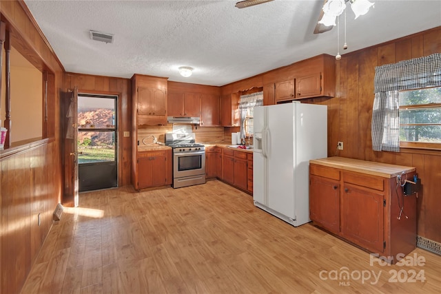 kitchen with gas stove, ceiling fan, light hardwood / wood-style flooring, white fridge with ice dispenser, and wood walls