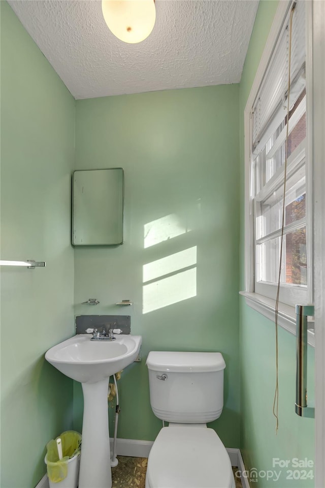 bathroom with a textured ceiling, toilet, and a wealth of natural light