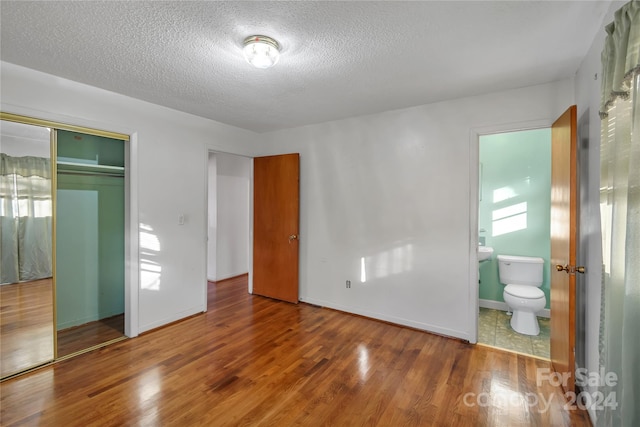 unfurnished bedroom featuring hardwood / wood-style flooring, ensuite bathroom, a textured ceiling, and a closet