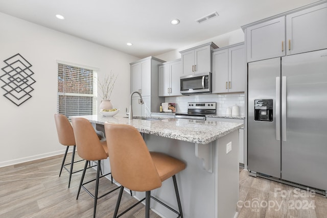 kitchen featuring a kitchen island with sink, sink, stainless steel appliances, and light hardwood / wood-style floors