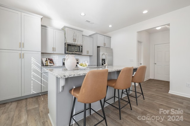 kitchen featuring light stone countertops, a kitchen breakfast bar, stainless steel appliances, dark hardwood / wood-style floors, and an island with sink