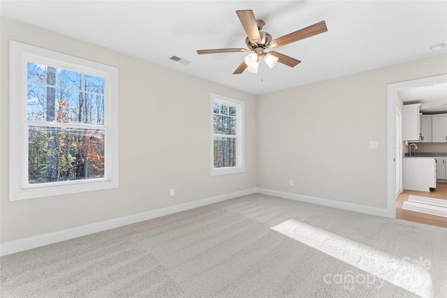 carpeted spare room featuring ceiling fan, plenty of natural light, and sink