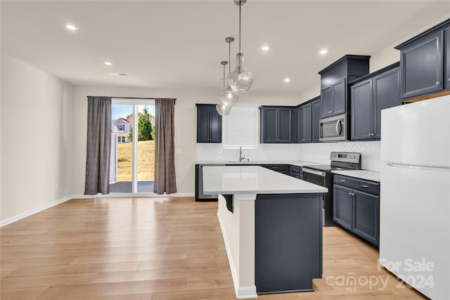 kitchen with sink, light wood-type flooring, appliances with stainless steel finishes, decorative light fixtures, and a kitchen island