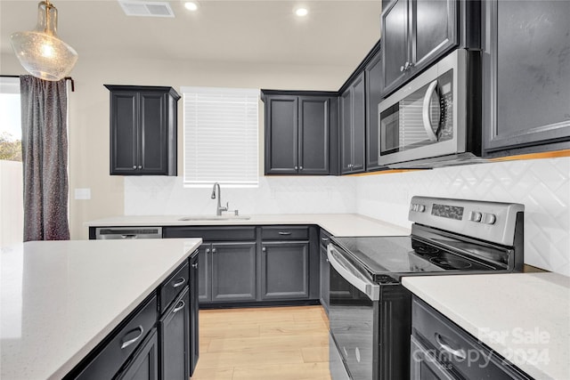 kitchen featuring backsplash, sink, light wood-type flooring, decorative light fixtures, and stainless steel appliances