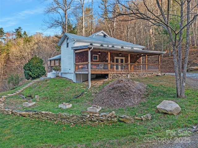 exterior space with ceiling fan, metal roof, a view of trees, and a lawn