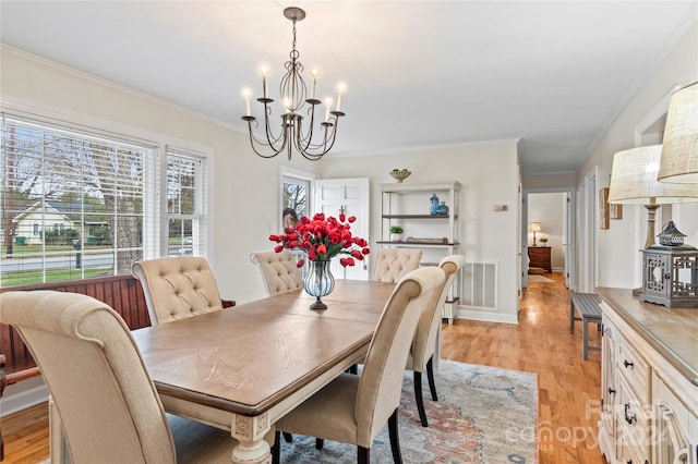 dining space with light wood-type flooring, ornamental molding, and a chandelier