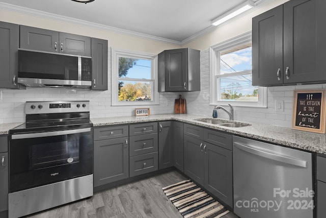 kitchen featuring light stone countertops, a wealth of natural light, ornamental molding, and appliances with stainless steel finishes