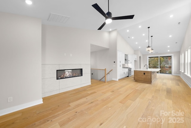 unfurnished living room featuring sink, ceiling fan, high vaulted ceiling, light hardwood / wood-style floors, and a tiled fireplace