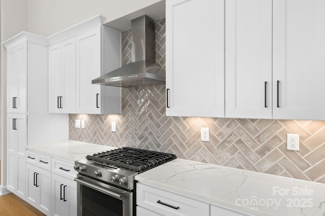 kitchen featuring light stone countertops, decorative backsplash, white cabinets, gas range, and wall chimney exhaust hood