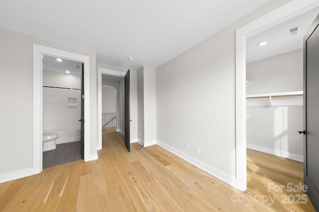 unfurnished bedroom with a closet, ensuite bathroom, and wood-type flooring