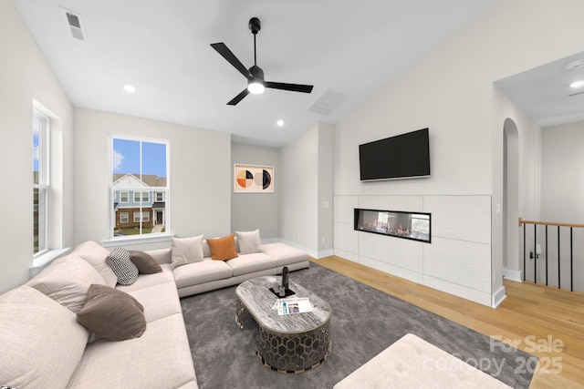 living room with hardwood / wood-style flooring, vaulted ceiling, ceiling fan, and a fireplace