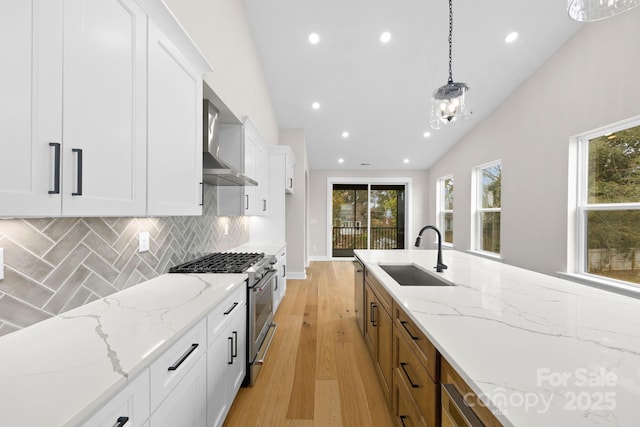 kitchen featuring wall chimney exhaust hood, hanging light fixtures, stainless steel appliances, white cabinetry, and a sink