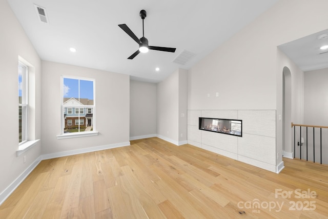 unfurnished living room featuring light wood-style floors, visible vents, vaulted ceiling, and a tiled fireplace