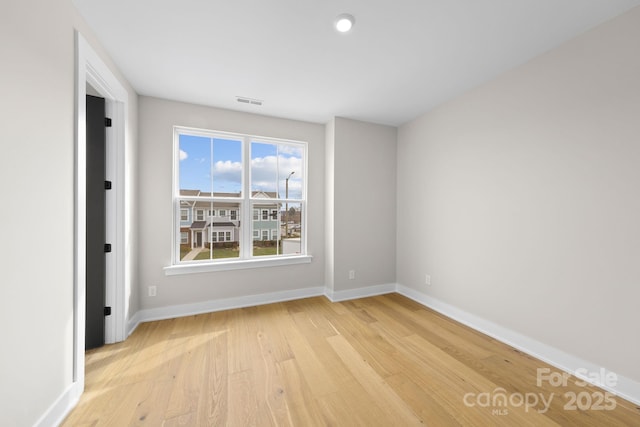 spare room featuring light wood-type flooring, visible vents, and baseboards