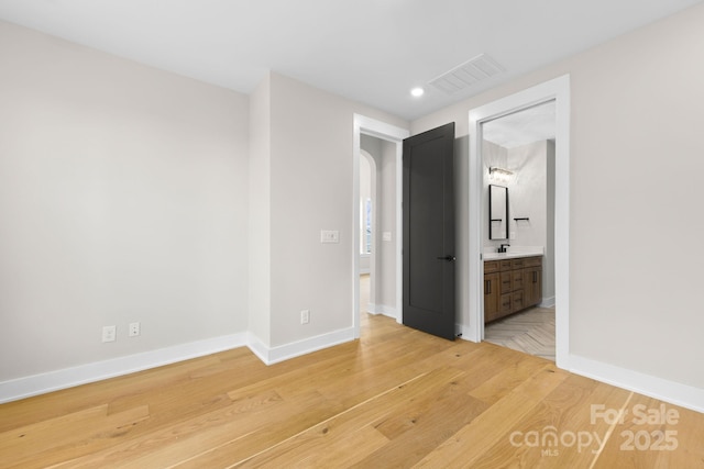 unfurnished bedroom featuring arched walkways, wood finished floors, and baseboards