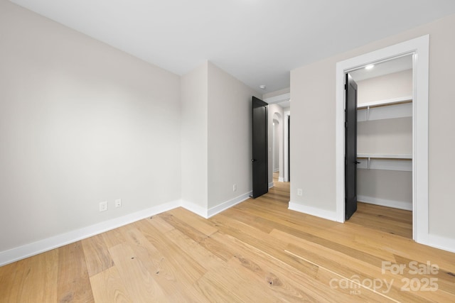 unfurnished bedroom featuring light wood-style floors, a walk in closet, a closet, and baseboards