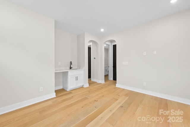 unfurnished room with arched walkways, recessed lighting, a sink, baseboards, and light wood finished floors