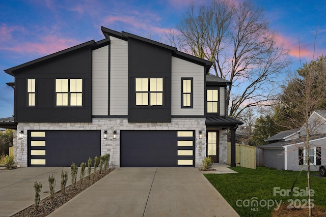 modern home with a garage, stone siding, concrete driveway, and a front yard