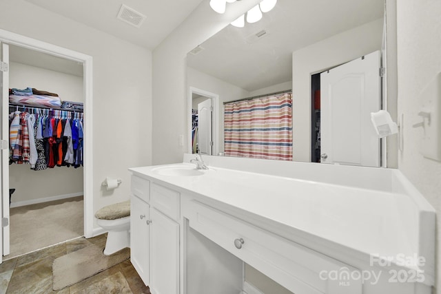 bathroom featuring visible vents, a walk in closet, toilet, and vanity