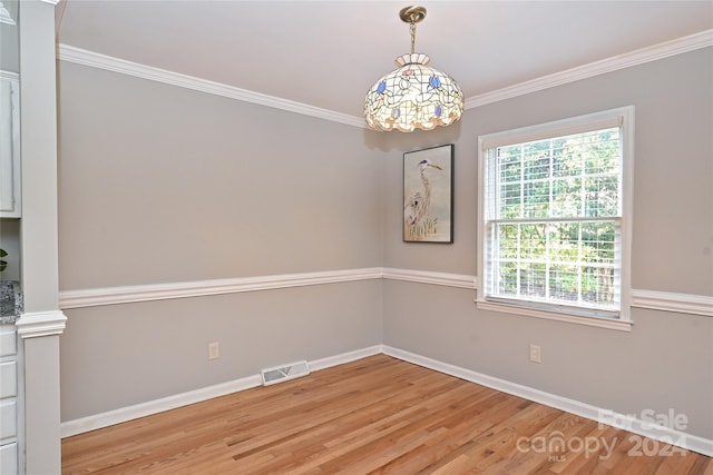 empty room with a chandelier, ornamental molding, and light wood-type flooring