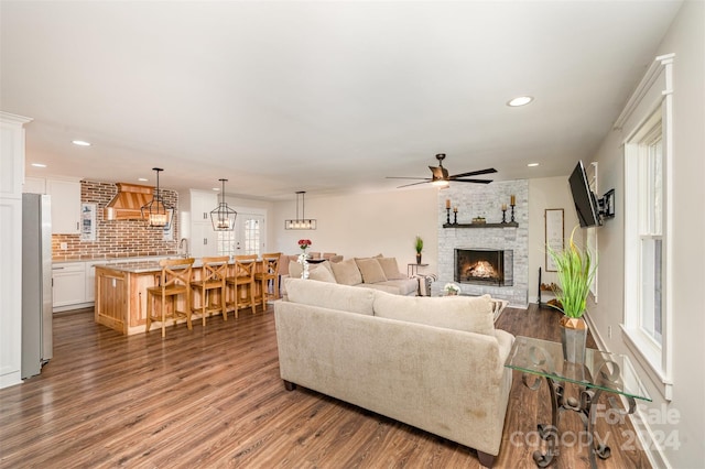 living room with dark hardwood / wood-style floors, a stone fireplace, ceiling fan, and sink