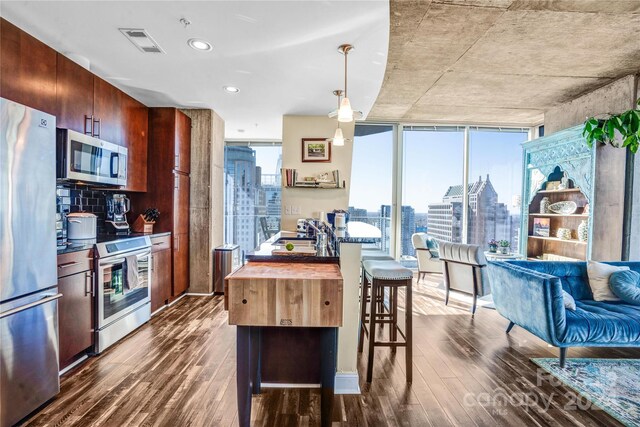 kitchen featuring a breakfast bar, wood counters, dark wood-type flooring, hanging light fixtures, and appliances with stainless steel finishes