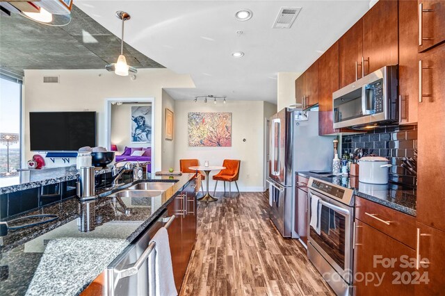 kitchen featuring backsplash, dark stone counters, stainless steel appliances, sink, and hardwood / wood-style flooring