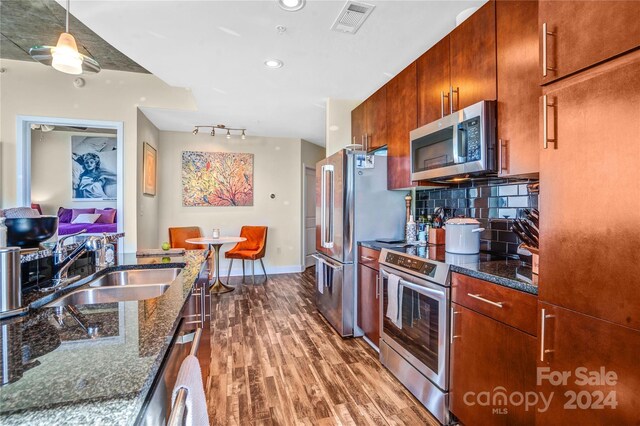 kitchen featuring sink, stainless steel appliances, backsplash, dark stone counters, and hardwood / wood-style flooring