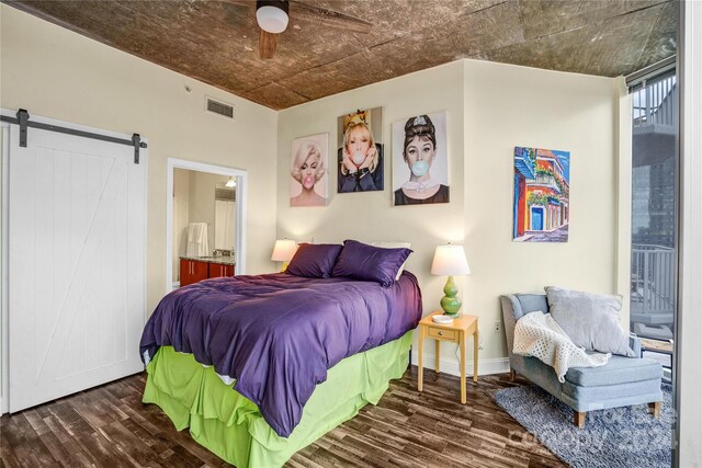 bedroom featuring connected bathroom, a barn door, ceiling fan, and dark hardwood / wood-style flooring