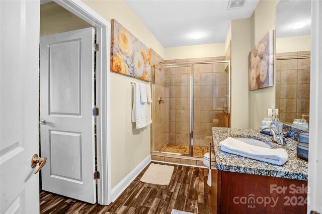 bathroom featuring vanity, wood-type flooring, a shower with shower door, and toilet