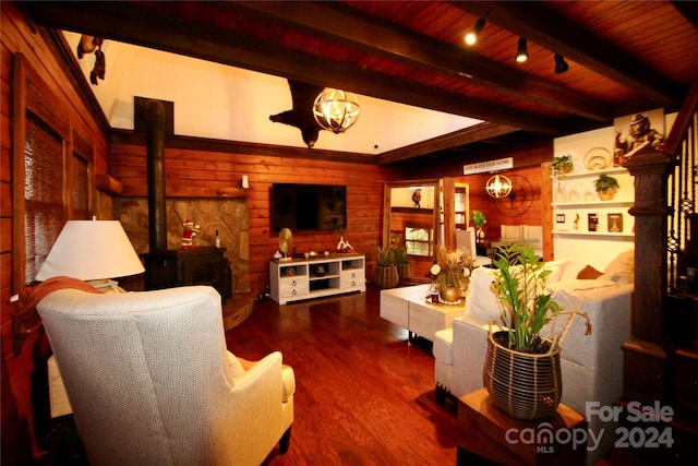 living room featuring wood walls, a wood stove, hardwood / wood-style flooring, a notable chandelier, and beam ceiling