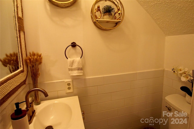 bathroom with toilet, sink, a textured ceiling, and tile walls