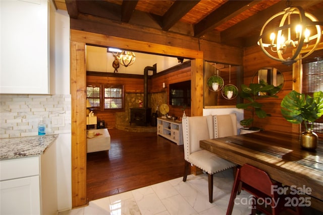 13538 Pine Harbor Rd, Charlotte, NC 28278 - dining area featuring a chandelier, wood walls, a wood stove, light marble finish flooring, and wood ceiling with exposed beams