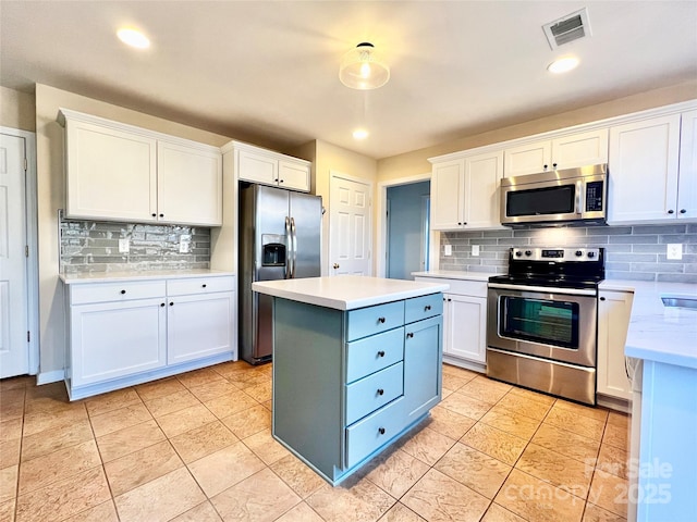 kitchen with white cabinets, appliances with stainless steel finishes, a kitchen island, and light tile patterned flooring