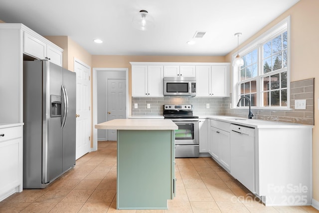 kitchen with sink, hanging light fixtures, stainless steel appliances, white cabinets, and a kitchen island